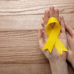 view-yellow-ribbon-with-human-hands-wooden-background-scaled