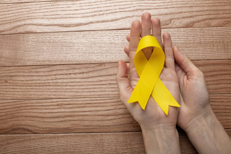 view-yellow-ribbon-with-human-hands-wooden-background-scaled